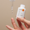 Hand hält geöffnetes Serum und Pipette zwischen den Fingern